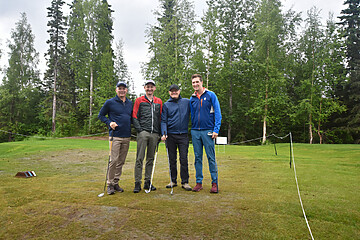 Four golfers enjoy a friendly game on a lush green golf course under an overcast sky.