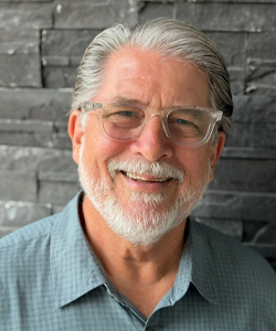 Warm, friendly portrait of a middle-aged man with silver hair and glasses.
