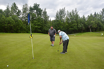 Men enjoying casual golf on a lush putting green under partly cloudy skies.