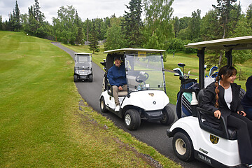 Golf course scene with golf carts, lush greenery, and players enjoying a leisurely game.