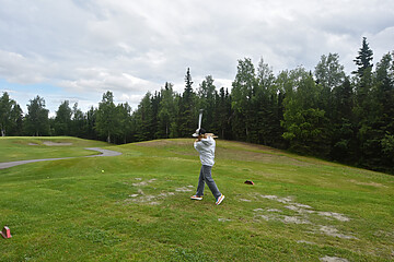 Golfer swinging on a lush golf course amid a serene natural landscape.