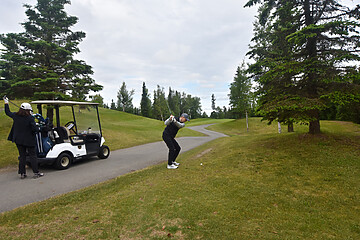 Golfer mid-swing on a lush golf course, surrounded by trees and a parked golf cart.