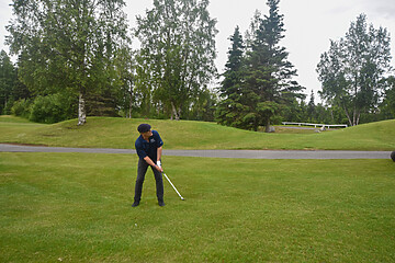 Golfer mid-swing on a scenic golf course, surrounded by lush greenery and trees.