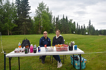 Women enjoying snacks and drinks at a cozy outdoor refreshment stand in nature.
